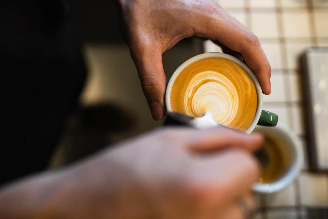 Top-down close-up view of a barista in the process of pouring a leaf pattern into a coffee cup. 