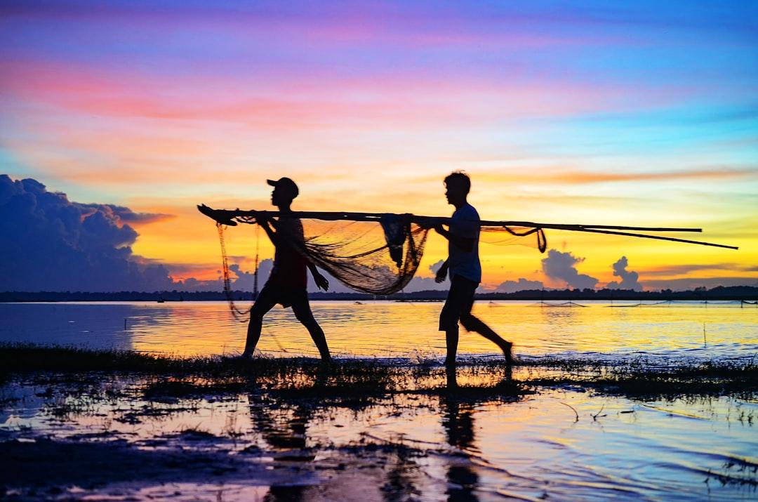 silhouette of 2 men holding fishing net on beach during sunset