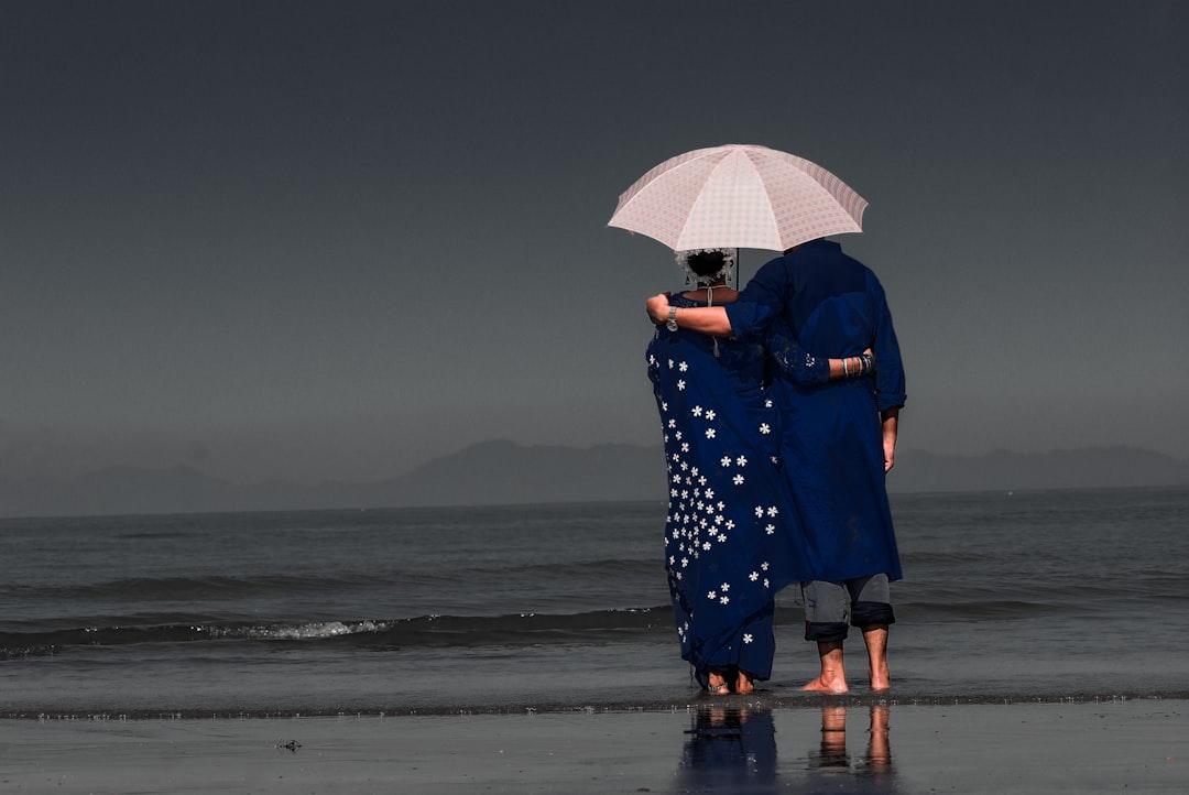 woman in blue and white floral dress holding umbrella walking on beach during daytime